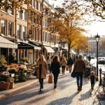 Drukke Amsterdamse gracht met diverse mensen die wandelen, fietsen en terrasjes bezoeken tussen traditionele Nederlandse huizen