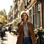 Professionele vrouw belt lopend door Amsterdamse straat met rode bakstenen gebouwen en geparkeerde fietsen