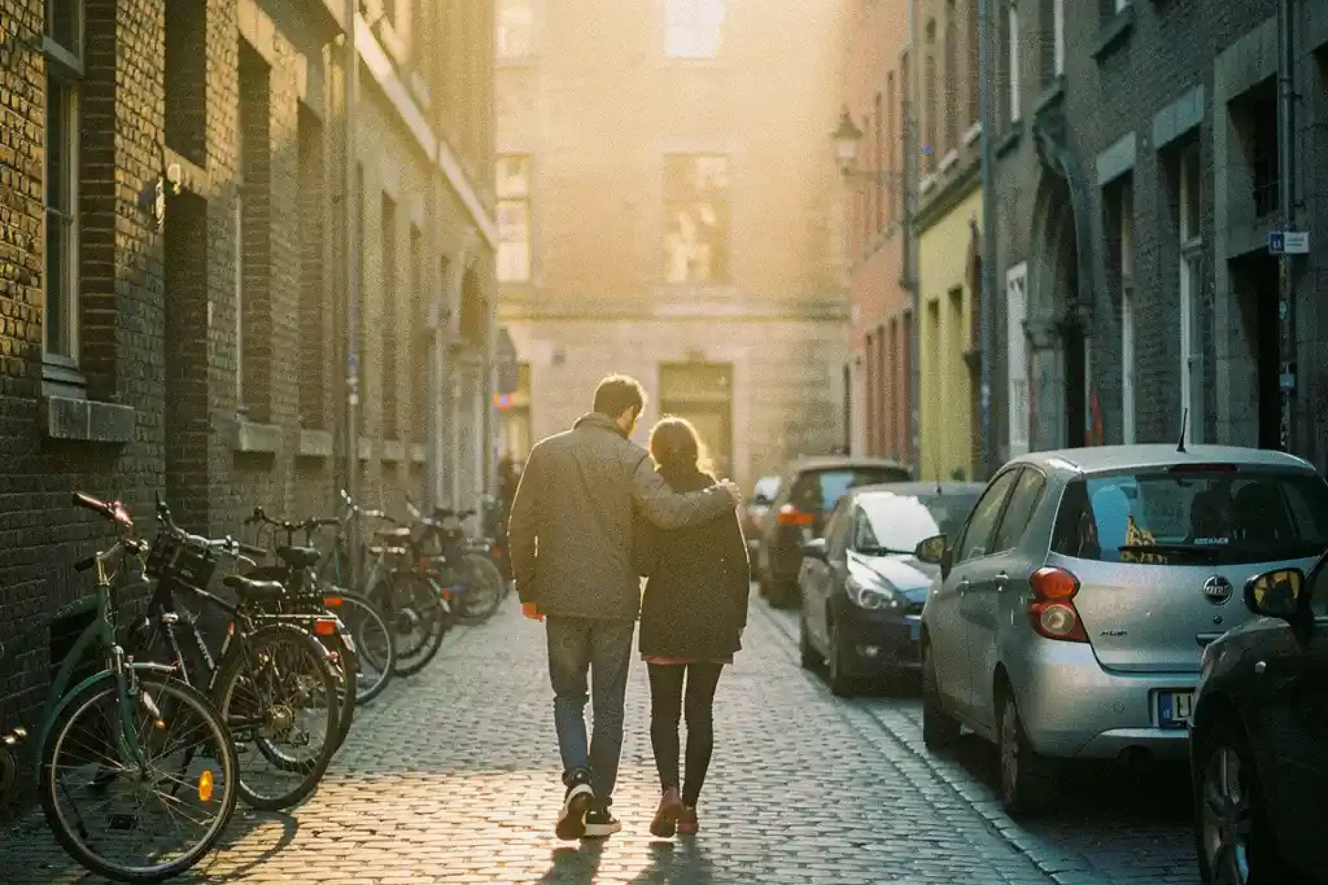 Twee mensen lopen samen door smalle kinderkopjesstraat in historisch Europees stadscentrum tijdens gouden uur