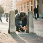 Persoon meet smalle parkeerruimte tussen betonnen palen op drukke Amsterdamse straat met bakstenen gebouwen op achtergrond