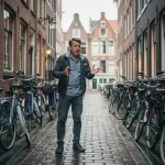 Gefrustreerde fietser op smalle Amsterdamse keistraat omringd door fietsen zonder parkeerruimte, hoge bakstenen gevels op de achtergrond.