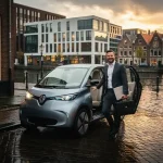 Elektrische stadsauto geparkeerd langs Utrechtse gracht, professional stapt uit met laptoptas op natte klinkerstraat.