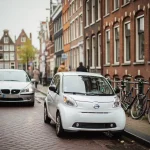 Kleine witte elektrische stadsauto parkeert in smalle Amsterdamse straat langs gracht, grote sedan rijdt rondjes op keienweg.
