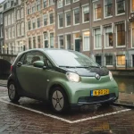 Compacte elektrische stadsauto geparkeerd op kasseistraat langs Amsterdams kanaal, natte straatkeien, smalle grachtenpanden op de achtergrond.