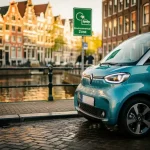 Elektrische stadsauto geparkeerd bij Amsterdamse grachtenbrug met groene milieuzonebordes, smalle klinkerstraat en weerspiegeling van grachtenpanden.