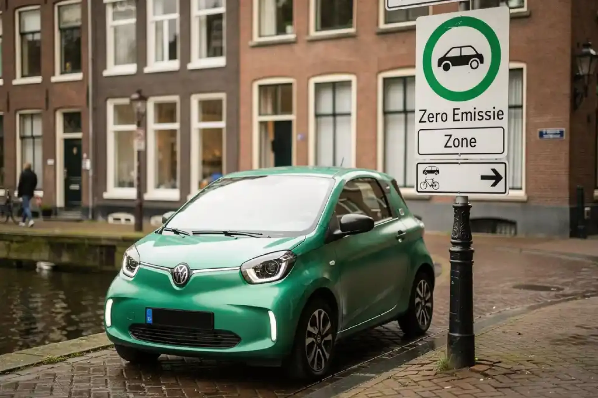 Kleine elektrische stadsauto bij ingang van een zero-emissiezone in Amsterdam, smalle gracht met bakstenen gevels op de achtergrond.