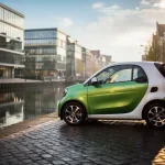 Compacte elektrische stadsauto op een smalle klinkerstraat in Den Haag, naast een gracht met moderne kantoorgebouwen in het water.