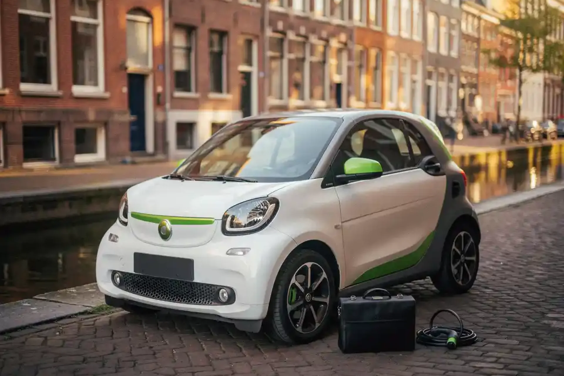Compacte elektrische stadsauto geparkeerd langs Rotterdamse gracht, met laadkabel en aktetas op de kinderkopjes, omringd door traditionele Nederlandse gevels.
