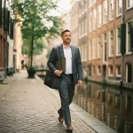 Professional met laptoptas wandelt zelfverzekerd door smal Amsterdams steegje langs historische grachtenpanden en kalm kanalwater.