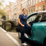 Thuiszorgverpleegkundige in marineblauwe scrubs stapt met medische tas uit elektrische auto op smalle Amsterdamse gracht bij ochtendlicht.