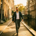 Zelfstandige professional met laptoptas wandelt langs Amsterdams gracht in middagzon, historische bakstenen gevels op achtergrond.